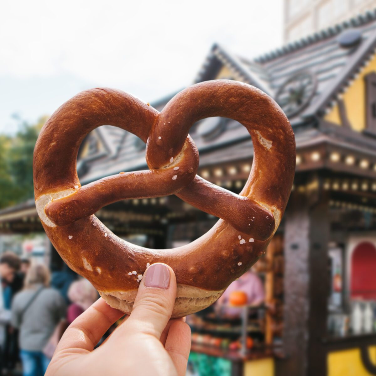 A girl or a young woman is holding a traditional German pretzel in the street. Oktoberfest festival in the background.